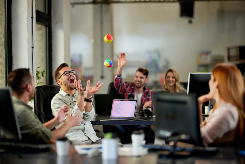 Group of cheerful programmers having fun while throwing balls during a break in the office.